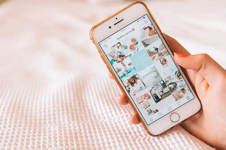 Person holding phone on bed, browsing Instagram